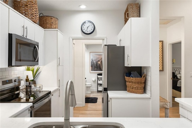 kitchen featuring decorative backsplash, appliances with stainless steel finishes, sink, light hardwood / wood-style flooring, and white cabinetry