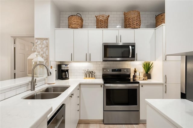 kitchen with backsplash, white cabinets, sink, light wood-type flooring, and appliances with stainless steel finishes