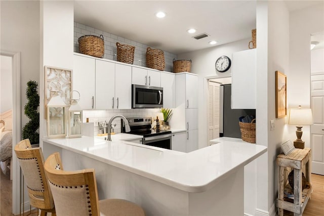 kitchen featuring a breakfast bar, kitchen peninsula, light hardwood / wood-style flooring, white cabinetry, and stainless steel appliances