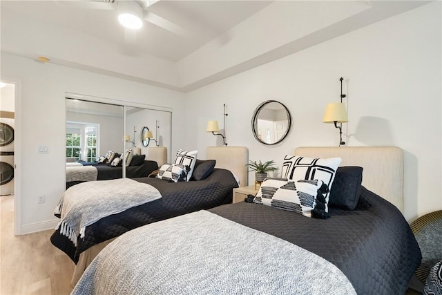 bedroom with a closet, hardwood / wood-style flooring, stacked washer / dryer, and ceiling fan