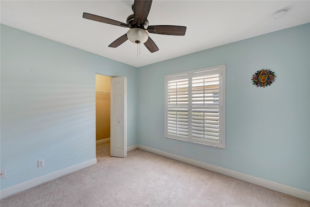 unfurnished bedroom with a closet, a spacious closet, light carpet, and ceiling fan