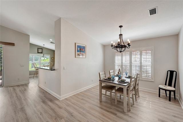 dining space featuring a wealth of natural light, light hardwood / wood-style flooring, vaulted ceiling, and a notable chandelier