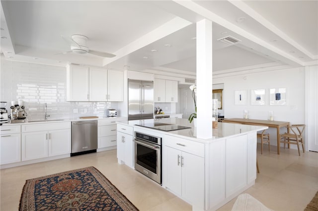 kitchen with white cabinetry, appliances with stainless steel finishes, a raised ceiling, a kitchen island, and sink