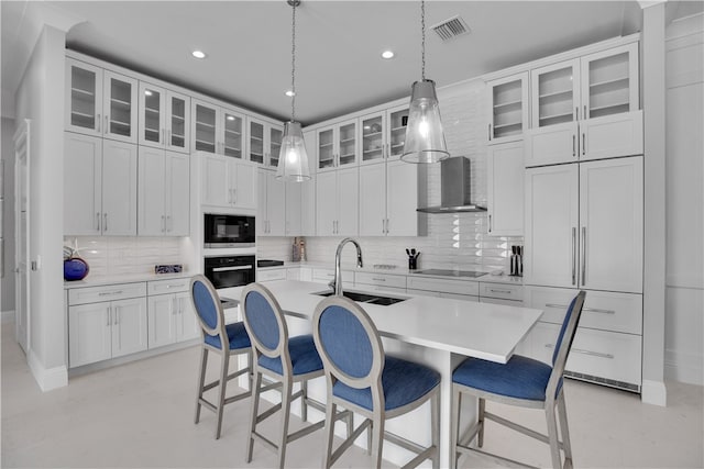 kitchen with black appliances, a center island with sink, decorative backsplash, sink, and wall chimney exhaust hood