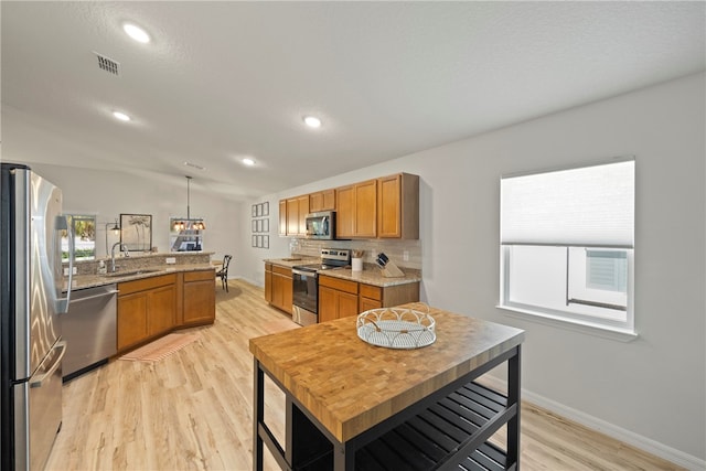 kitchen featuring pendant lighting, light wood-type flooring, appliances with stainless steel finishes, and vaulted ceiling