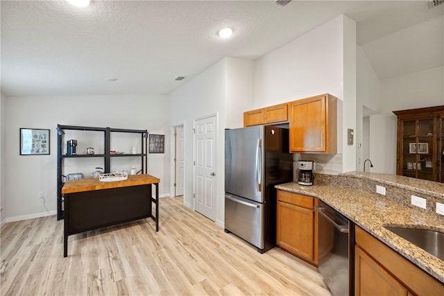 kitchen with light stone counters, appliances with stainless steel finishes, a textured ceiling, high vaulted ceiling, and light hardwood / wood-style floors