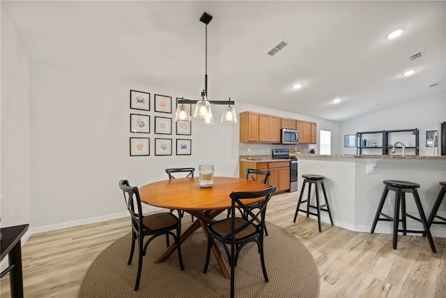 dining area with light wood-type flooring and vaulted ceiling