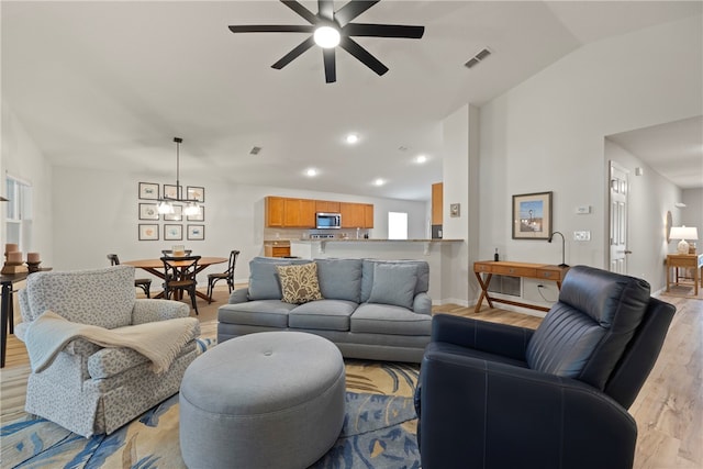 living room with light wood-type flooring, ceiling fan with notable chandelier, and vaulted ceiling