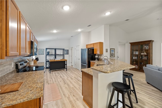 kitchen featuring stainless steel appliances, kitchen peninsula, a breakfast bar area, sink, and light stone countertops