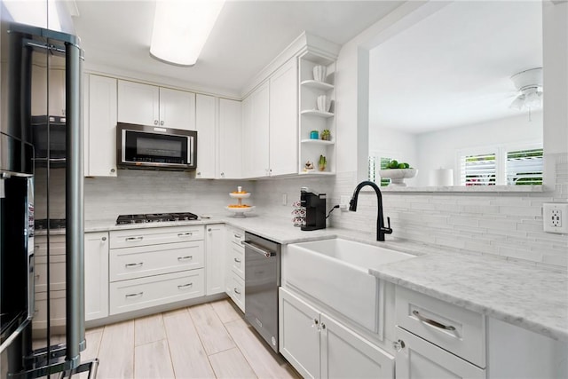 kitchen with sink, light stone counters, white cabinets, stainless steel appliances, and backsplash