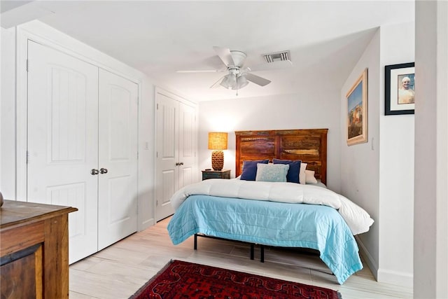 bedroom with two closets, ceiling fan, and light hardwood / wood-style flooring