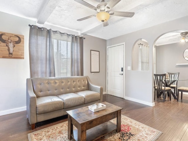 living room featuring beamed ceiling, ceiling fan, dark wood-type flooring, and a textured ceiling