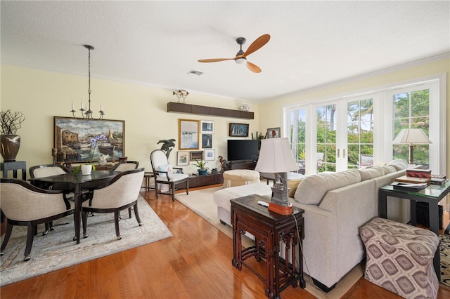 living room featuring ceiling fan with notable chandelier, a textured ceiling, hardwood / wood-style floors, crown molding, and french doors