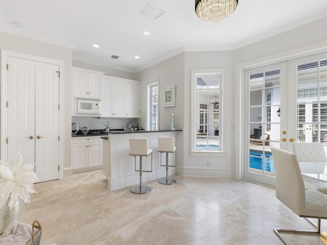 7 Beachside Dr, Vero Beach, FL 32963 - kitchen featuring white microwave, crown molding, white cabinets, a breakfast bar, and dark countertops