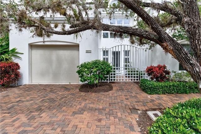 view of front of house featuring decorative driveway, an attached garage, and stucco siding