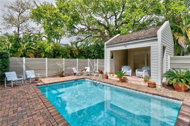 view of pool with a patio area, fence, and an outbuilding