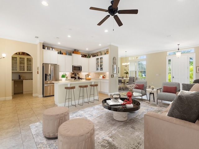 tiled living room with ceiling fan with notable chandelier and crown molding