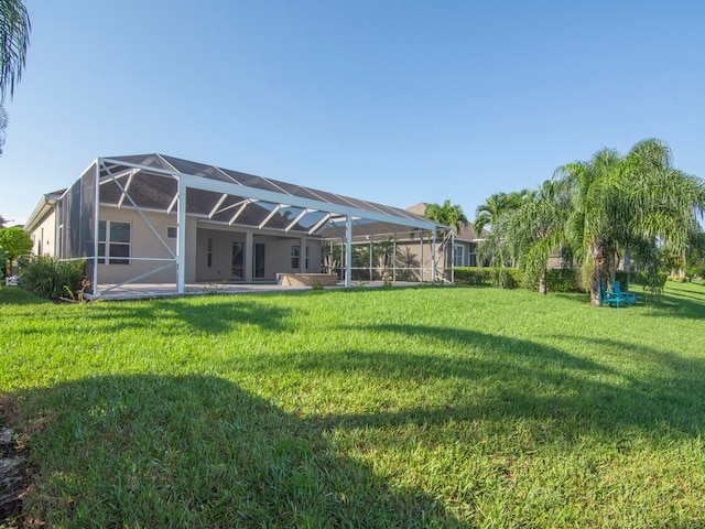 back of property featuring glass enclosure, a lawn, and a patio