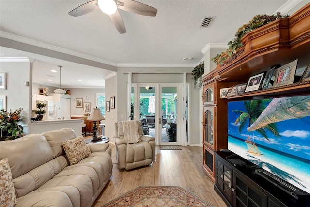 living room with a textured ceiling, light wood-type flooring, ceiling fan, and ornamental molding