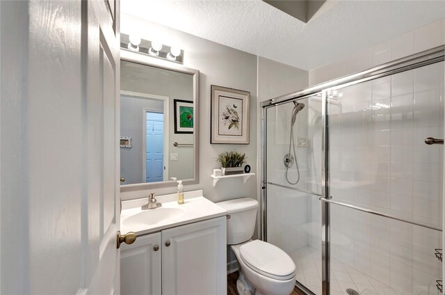 bathroom with vanity, a textured ceiling, toilet, and a shower with shower door