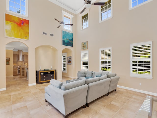 tiled living room with ceiling fan, a wealth of natural light, ornamental molding, and a towering ceiling