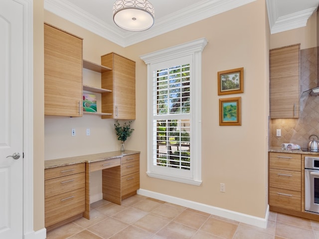 kitchen with built in desk, ornamental molding, backsplash, light tile patterned floors, and light stone countertops