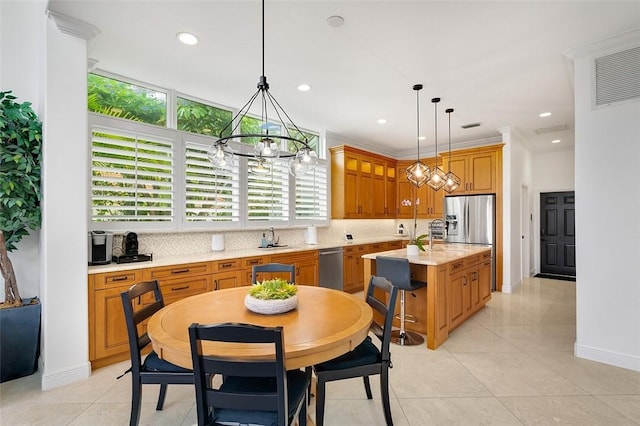 kitchen featuring light tile patterned floors, appliances with stainless steel finishes, hanging light fixtures, light stone countertops, and a center island with sink