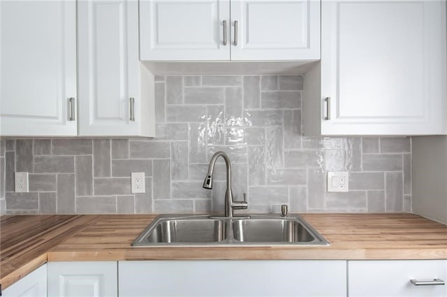 kitchen with wooden counters, backsplash, sink, and white cabinets