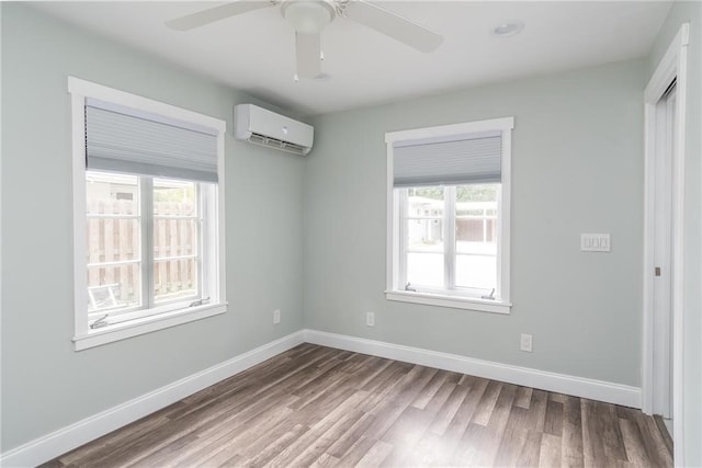 spare room with a wall unit AC, hardwood / wood-style flooring, ceiling fan, and plenty of natural light