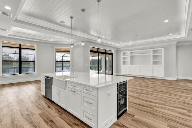 kitchen with decorative light fixtures, an island with sink, sink, white cabinets, and beverage cooler