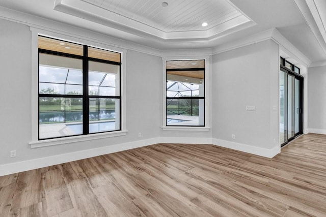 empty room with a raised ceiling, ornamental molding, and light hardwood / wood-style flooring