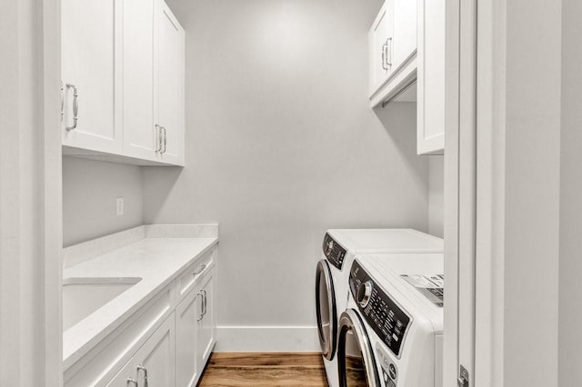 clothes washing area with sink, light hardwood / wood-style floors, cabinets, and washing machine and clothes dryer