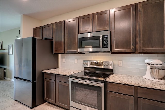 kitchen featuring appliances with stainless steel finishes, dark brown cabinetry, light tile patterned floors, light stone countertops, and decorative backsplash