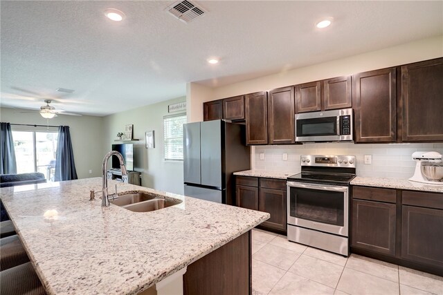 kitchen featuring a kitchen bar, stainless steel appliances, a center island with sink, decorative backsplash, and sink