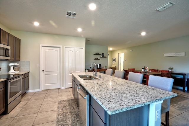 kitchen with tasteful backsplash, appliances with stainless steel finishes, sink, an island with sink, and a kitchen breakfast bar