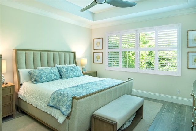 bedroom with ornamental molding, light hardwood / wood-style flooring, ceiling fan, and a tray ceiling