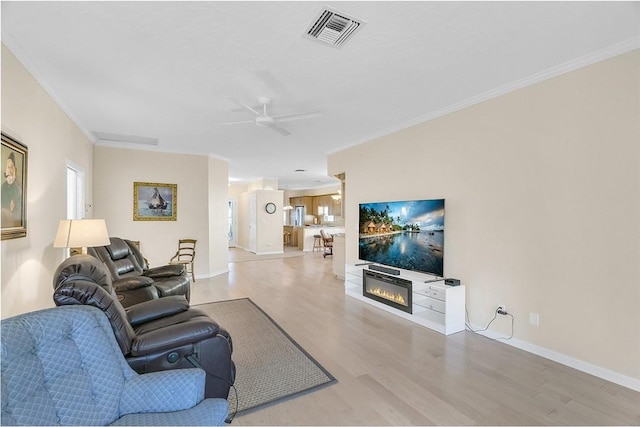 living area featuring visible vents, crown molding, baseboards, light wood-style flooring, and a ceiling fan