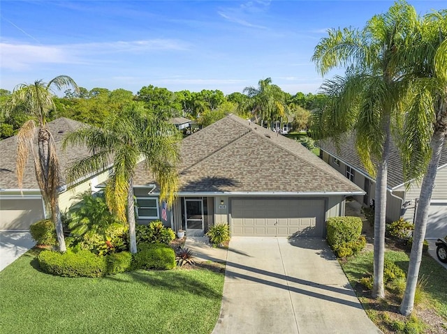 view of front facade with a front lawn, an attached garage, roof with shingles, and driveway