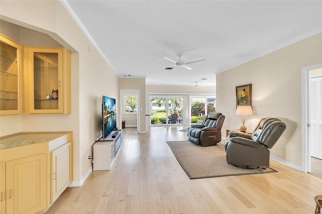 living area with light wood-style flooring, baseboards, ceiling fan, and ornamental molding