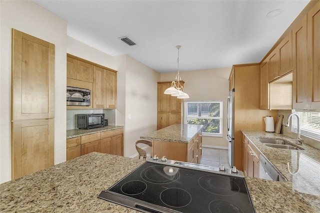 kitchen featuring light stone counters, visible vents, stainless steel appliances, a sink, and a center island