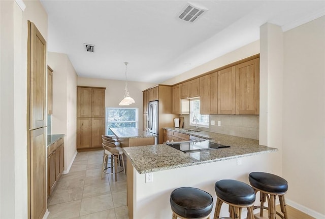 kitchen featuring a peninsula, light stone counters, visible vents, and a sink