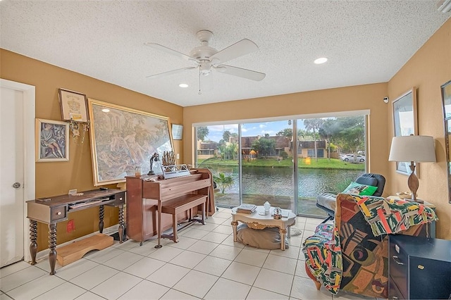 interior space with light tile patterned floors, ceiling fan, a textured ceiling, and a water view