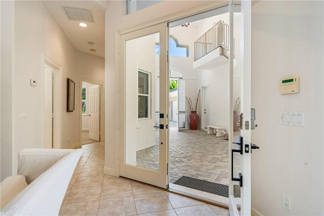 doorway with light tile patterned floors, baseboards, visible vents, a high ceiling, and recessed lighting