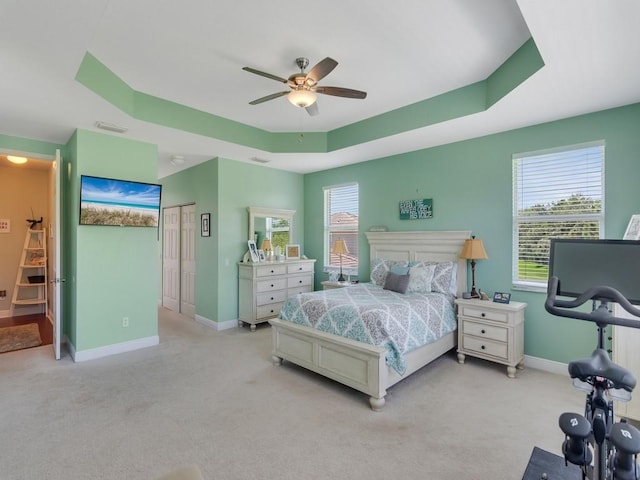 bedroom featuring a tray ceiling, baseboards, and light colored carpet