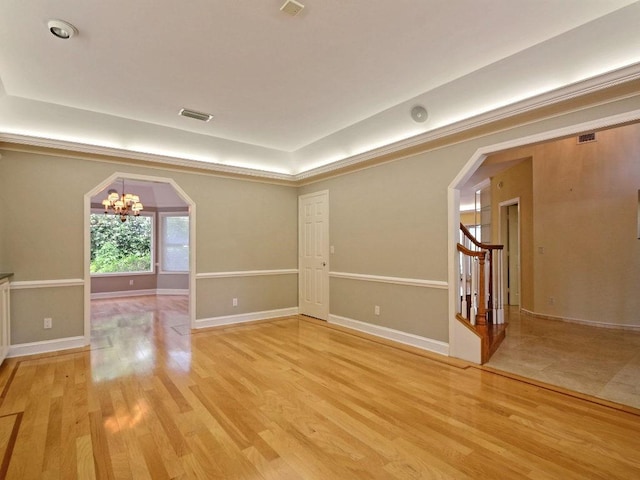 unfurnished room with a chandelier, light wood-type flooring, arched walkways, and stairs