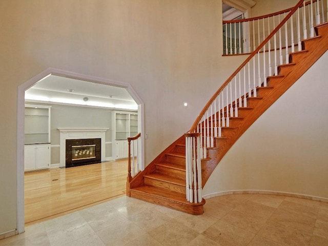 staircase with a high end fireplace, a towering ceiling, and baseboards