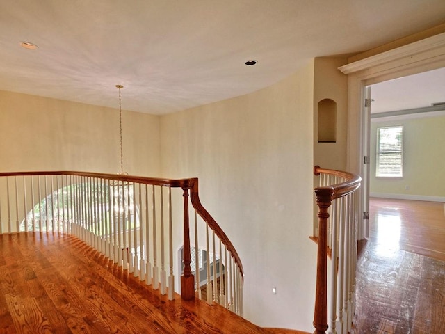 corridor with wood finished floors, an upstairs landing, and baseboards