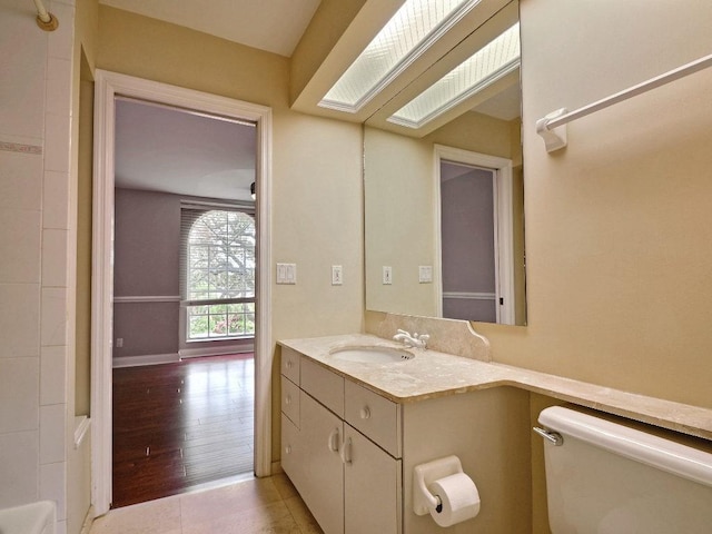 bathroom featuring a skylight, vanity, toilet, and baseboards