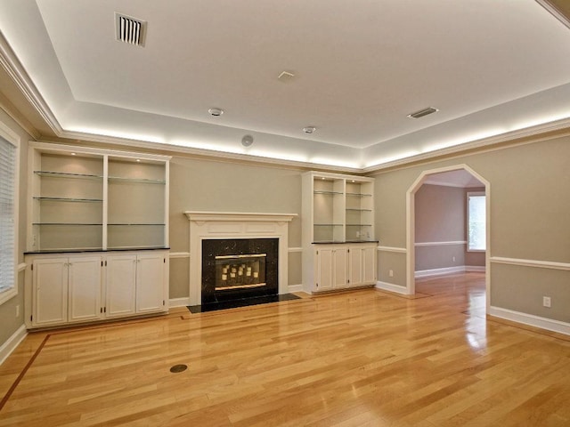 unfurnished living room featuring arched walkways, a premium fireplace, visible vents, light wood finished floors, and a raised ceiling