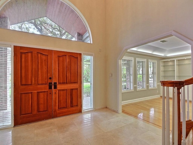 entrance foyer with a towering ceiling, baseboards, visible vents, and a tray ceiling